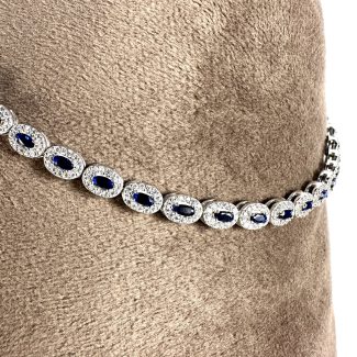 „Colier Safir Diamonds” este un colier uimitor de argint, cu pietre prețioase de safir în formă ovală, fiecare înconjurată elegant de mici diamante, frumos prezentate pe un fundal moale de țesătură bej.