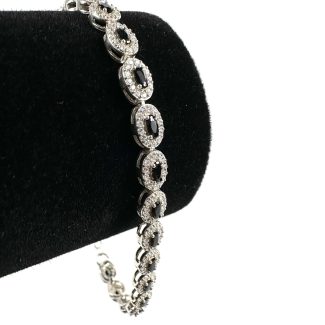 Brățară Safir Black Diamonds, o brățară de argint cu zale circulare împodobite cu diamante mici, strălucitoare, este prezentată elegant pe un suport de catifea neagră pe un fundal alb simplu.