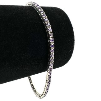 Brățară Tennis Purple, împodobită cu pietre prețioase violet strălucitoare, este expusă pe un suport de catifea neagră. Forma sa elegantă, rotunjită, evidențiază designul său elegant pe fundalul simplu.